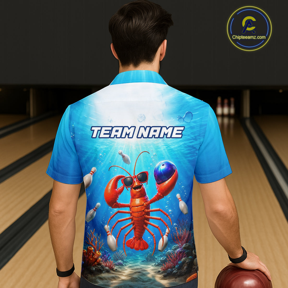 Person wearing a blue bowling shirt with a lobster design and 'TEAM NAME' text in a bowling alley.
