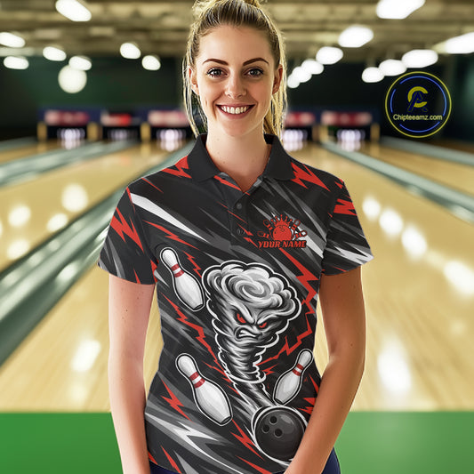 A woman wearing a custom bowling black and red womens polo shirt with a printed tornado and bowling pins graphic, standing in front of a blurred bowling alley background.
