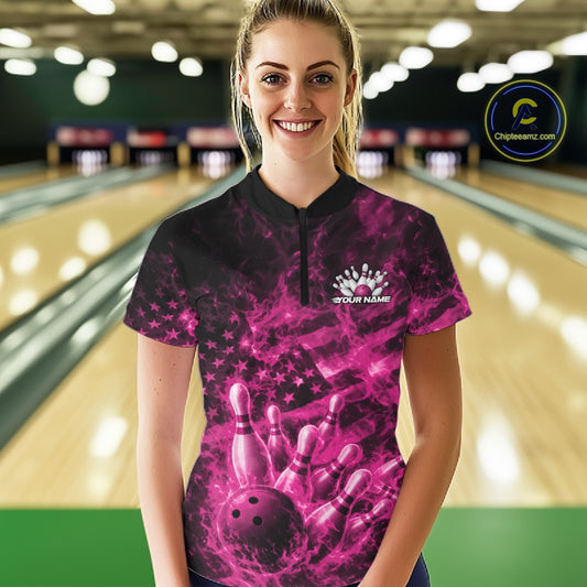 Female model at a bowling alley wearing a black and pink quarter-zip featuring fiery bowling action artwork and an American flag backdrop.