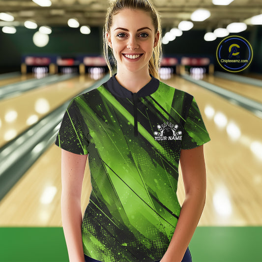Woman wearing a green and black bowling shirt with a logo in a bowling alley.
