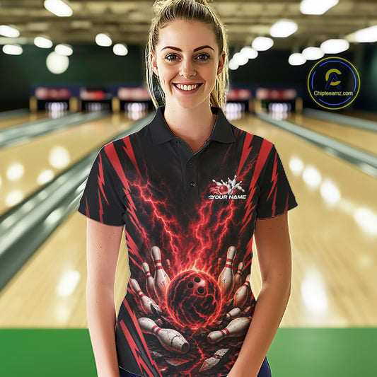 A woman stands in a bowling alley wearing a black short-sleeve polo shirt with a red and black lightning-bolt bowling graphic and a white 'YOUR NAME' placeholder logo on the chest.