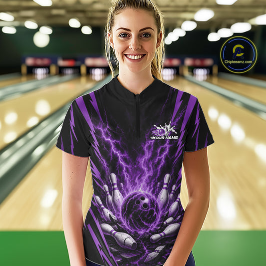 A woman wearing a black and purple bowling-themed short-sleeve shirt with a lightning-bolt hand graphic, standing in front of a blurred bowling alley background.