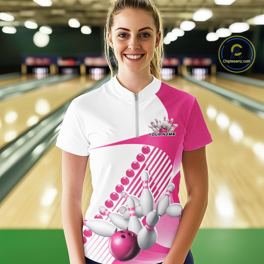 Female model wearing a white and pink bowling quarter zip featuring flowing geometric stripe artwork and a dynamic bowling strike motif at the bowling lane.