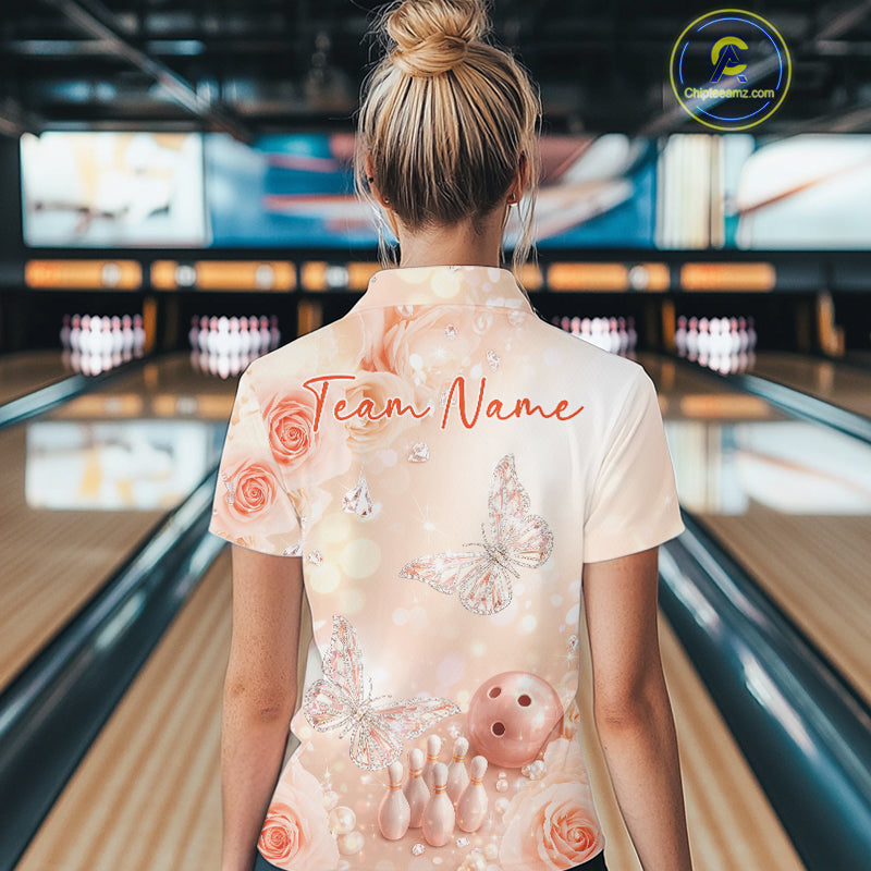 Back view of a female model in a bowling alley wearing a quarter-zip shirt featuring pastel butterfly artwork above bowling pins and a bowling ball.