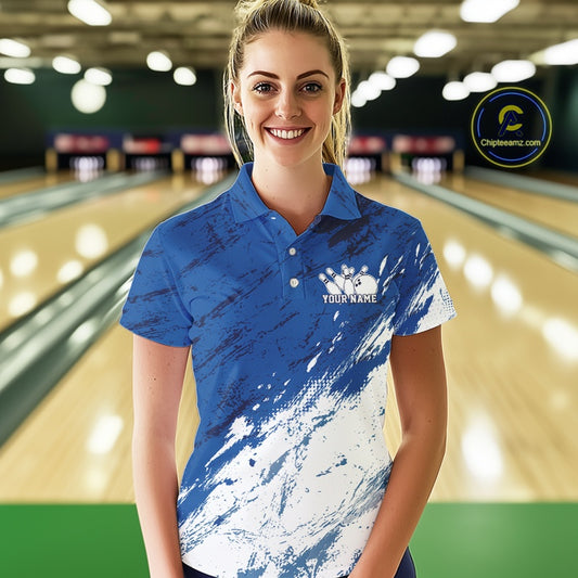 Front view of a female bowler wearing a white and blue bowling polo shirt with a splatter-inspired sports jersey design in a bowling lane