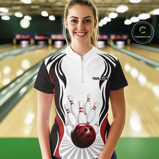 Front view of a female model inside a bowling center wearing a white, black, and red bowling quarter-zip shirt with bowling ball striking pins artwork.