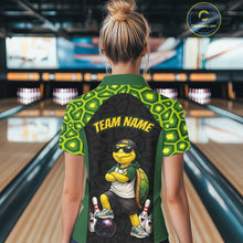 Load image into Gallery viewer, A woman viewed from behind wearing a green and black short-sleeve bowling-themed quarter-zip shirt with a cartoon turtle graphic and 'TEAM NAME' text on the back, standing in a bowling alley.