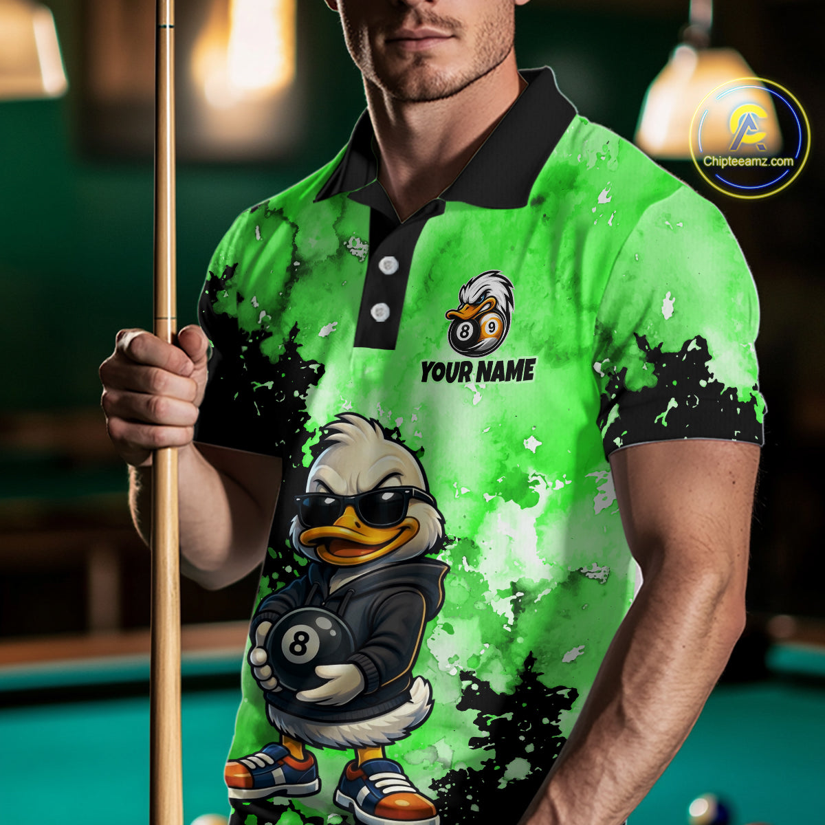 A man wearing a bright green and black custom-printed polo shirt with a cartoon duck character holding an 8-ball, holding a pool cue in a dimly lit pool hall. 
