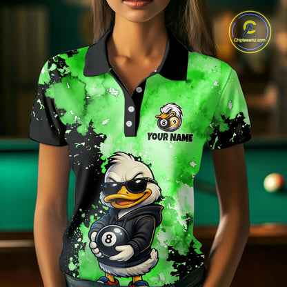 A woman wearing a short-sleeve polo shirt with a bright green and black splatter design, featuring a cartoon duck wearing sunglasses and holding an 8-ball, with the text 'YOUR NAME' and a bird-and-ball logo on the chest. The background is a blurred pool room.