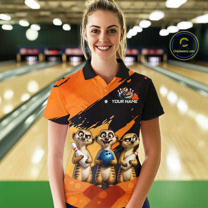 A woman standing in a bowling alley wearing a custom orange and black short-sleeve polo shirt with a graphic of three cartoon meerkats holding bowling balls and a 'YOUR NAME' customization option on the chest. 