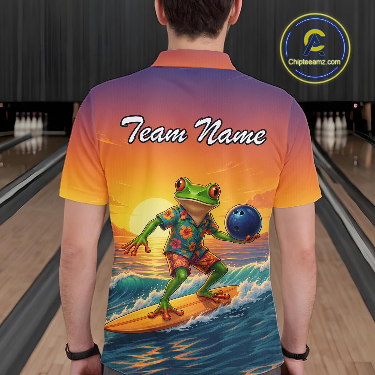 A person viewed from behind wearing a short-sleeve bowling shirt with a colorful sunset gradient and a large graphic of a green frog surfing while holding a bowling ball. The shirt has 'Team Name' printed across the upper back.