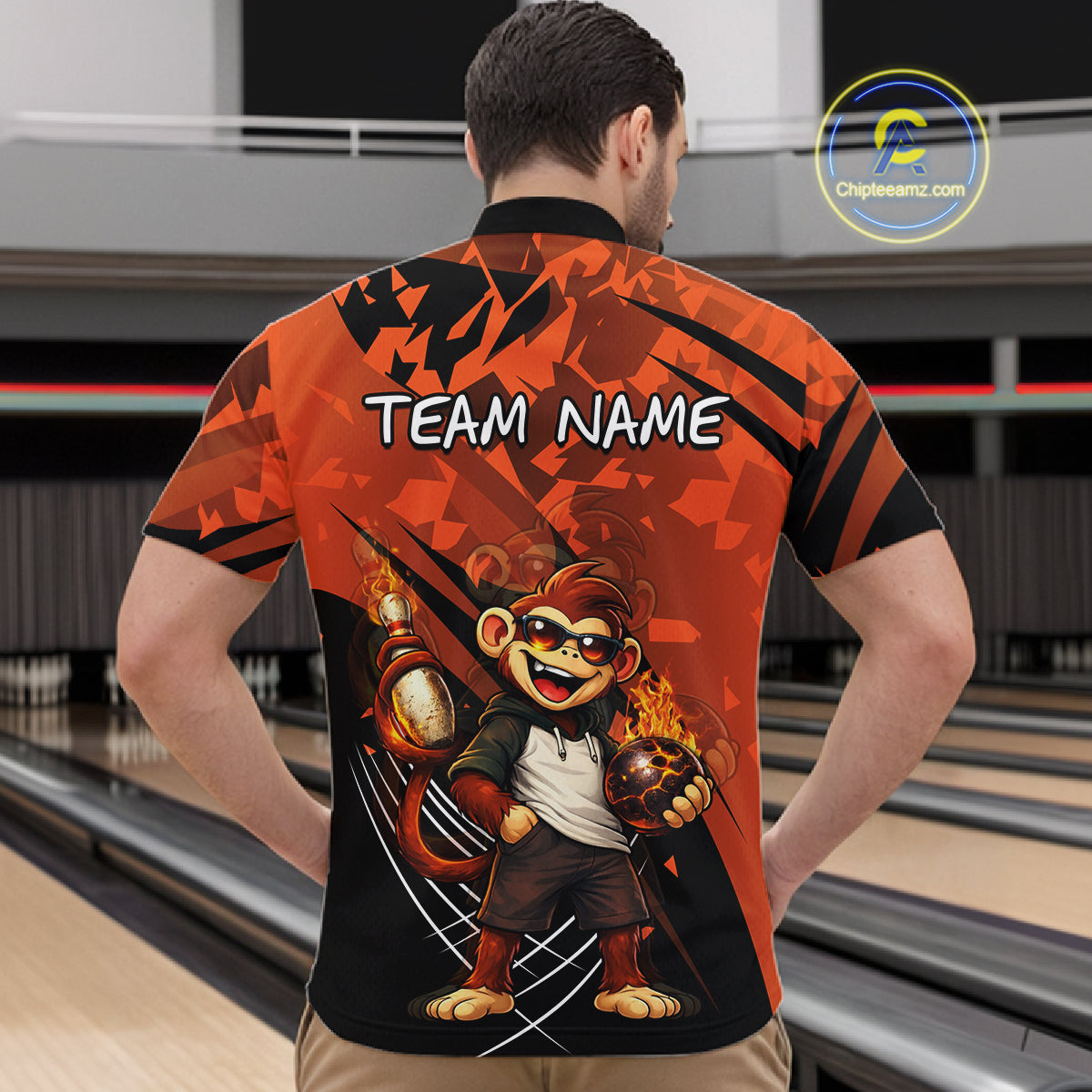 A man viewed from behind wearing a short-sleeve bowling shirt with a bold orange and black graphic design featuring a cartoon monkey and the text 'TEAM NAME' on the back. Bowling lanes are visible in the background, and a 'Chipteamz.