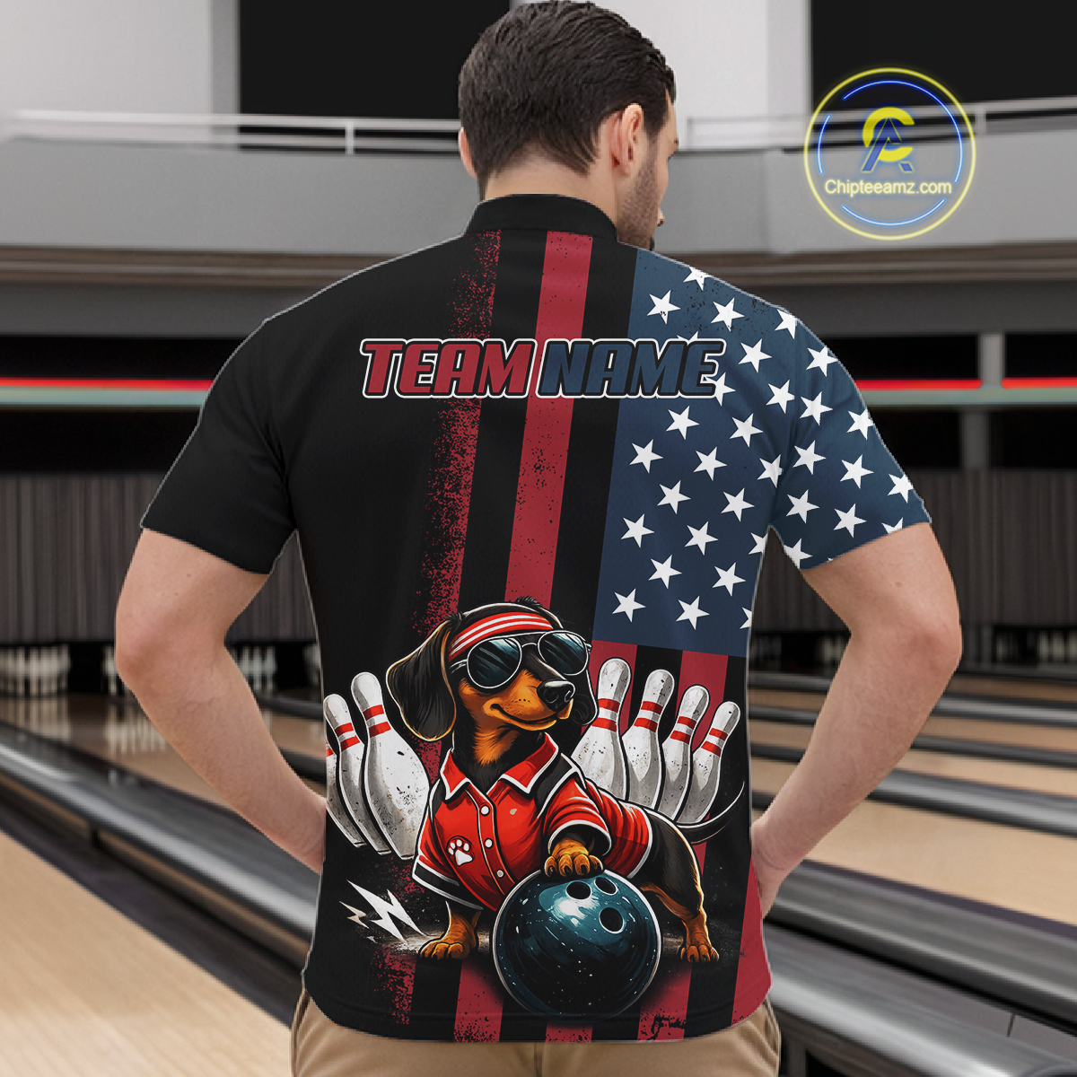 Person wearing a black shirt with a graphic design of a dachshund bowling, American flag, and 'Team Name' text in a bowling alley.