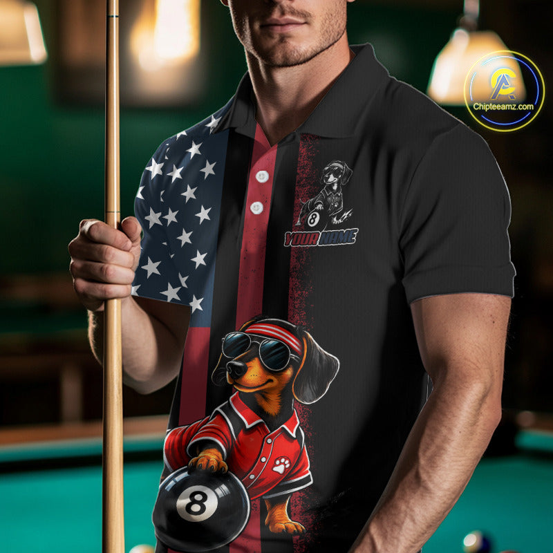 A man in a poolroom wearing a black polo shirt with a custom graphic print featuring a dachshund wearing sunglasses and holding a 8-ball, alongside an American flag pattern on the sleeve. He is holding a pool cue.