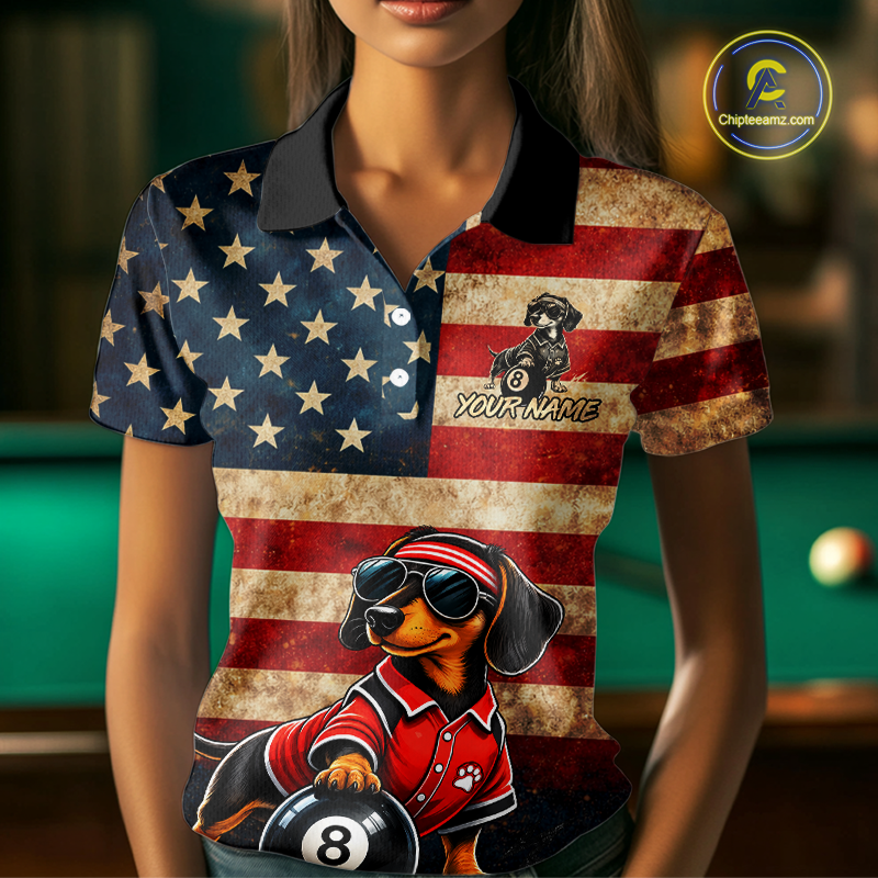A woman wearing a short-sleeve polo shirt with a distressed American flag design and a dachshund billiards graphic. The shirt has a black collar and white buttons