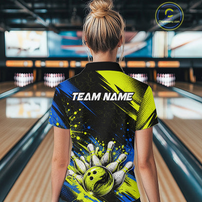 A woman viewed from behind in a bowling alley, wearing a short-sleeve collared shirt with a bold bowling-themed graphic print. The shirt features a black background with bright yellow and blue paint splatter effects, a bowling pin-and-ball design near the hem, and the text 'TEAM NAME' across the upper back.