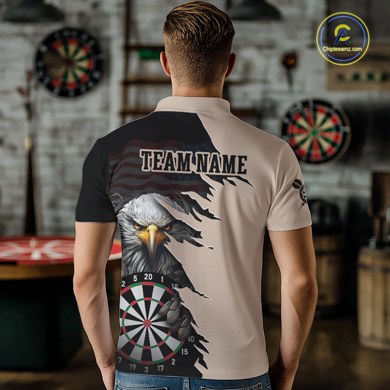 Person wearing a beige and black darts polo featuring a bald eagle, torn-flag graphics, dartboard designs, and custom team text.