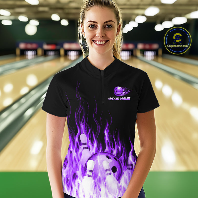 Person wearing a black bowling shirt with purple flames and a logo on a bowling alley background