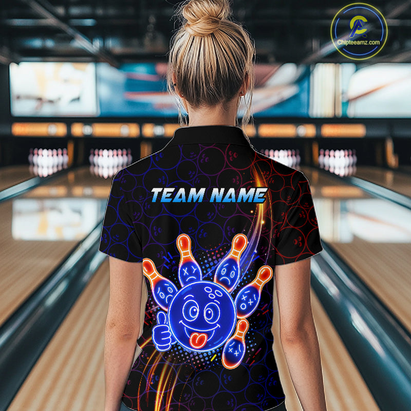 Woman standing in a bowling alley wearing a black neon-style bowling polo shirt with a glowing blue cartoon bowling ball mascot, fiery orange pin graphics, and custom name text.