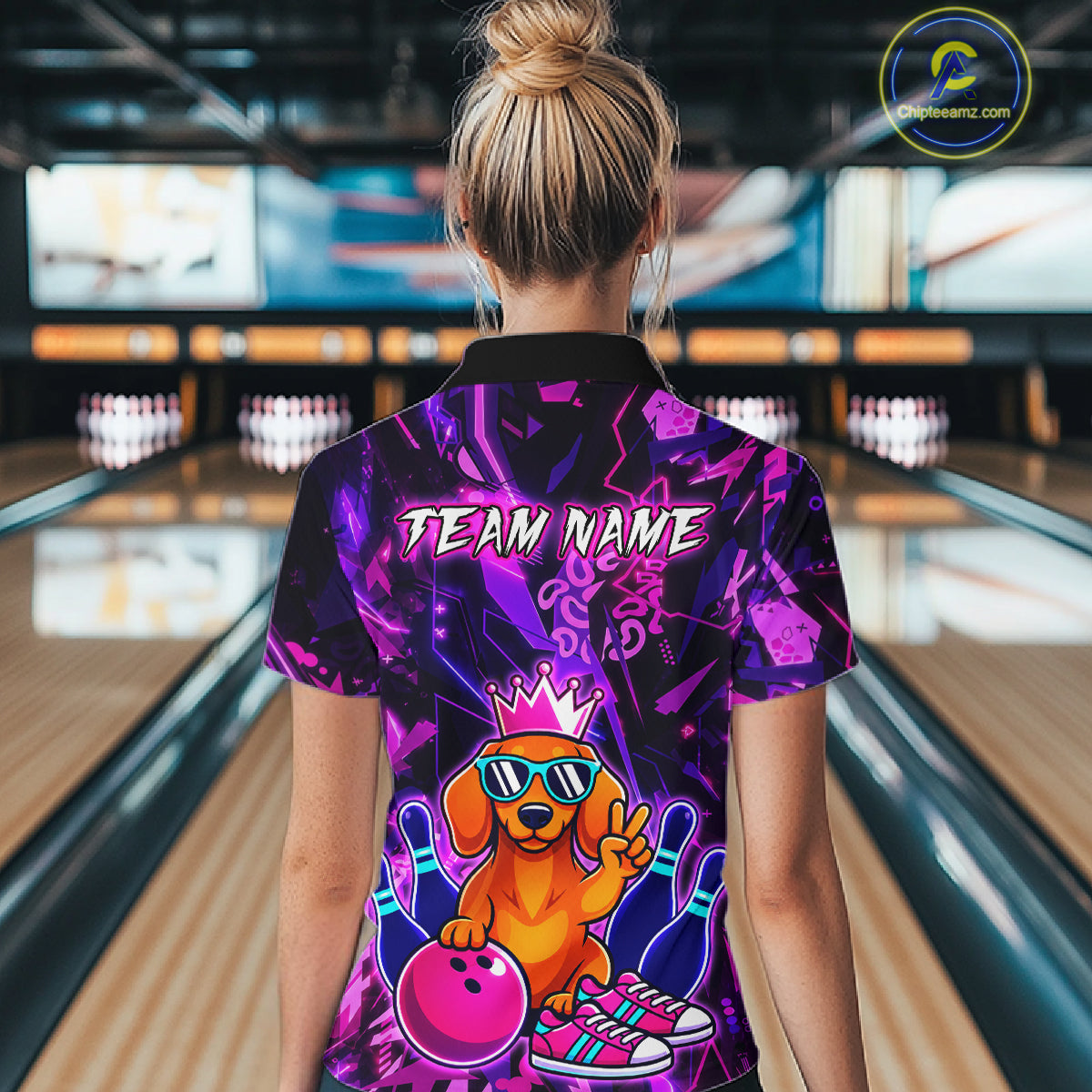 Woman wearing a black and purple bowling polo shirt featuring a cartoon dachshund wearing sunglasses and a crown, holding a pink bowling ball, with custom team name text.