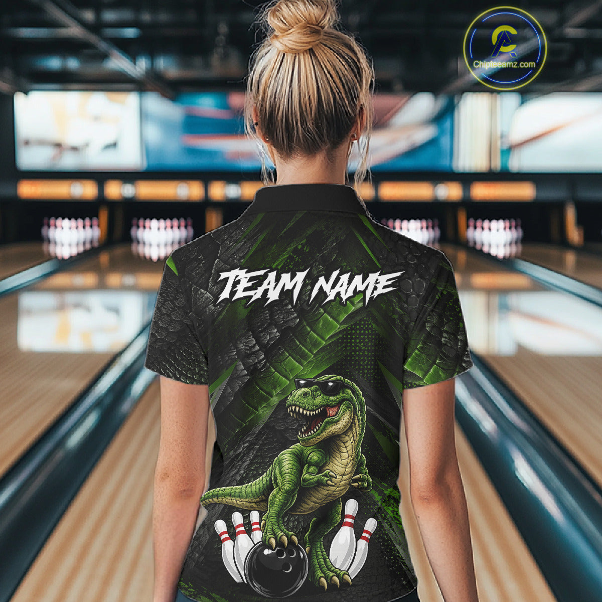 Women wearing bowling quarter zip shirt featuring a dinosaur standing among bowling pins and ball artwork on black green textured background.