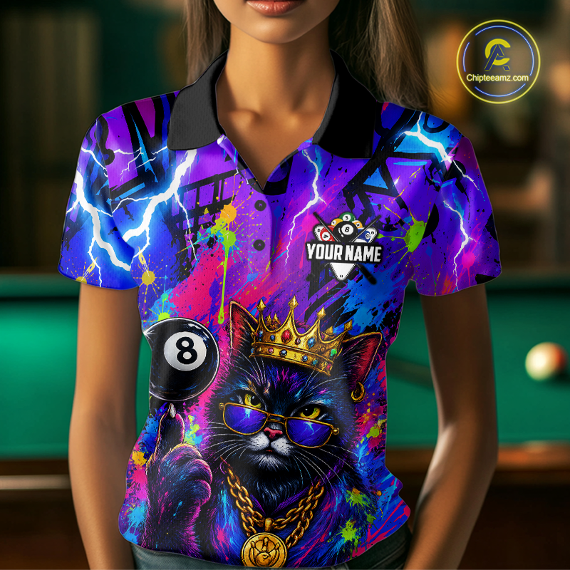 A woman wearing a short-sleeve polo shirt with a vibrant, colorful graphic print of a black cat wearing a gold crown and sunglasses, holding a black 8-ball. The shirt features purple, blue, and pink paint splatter patterns with lightning accents.