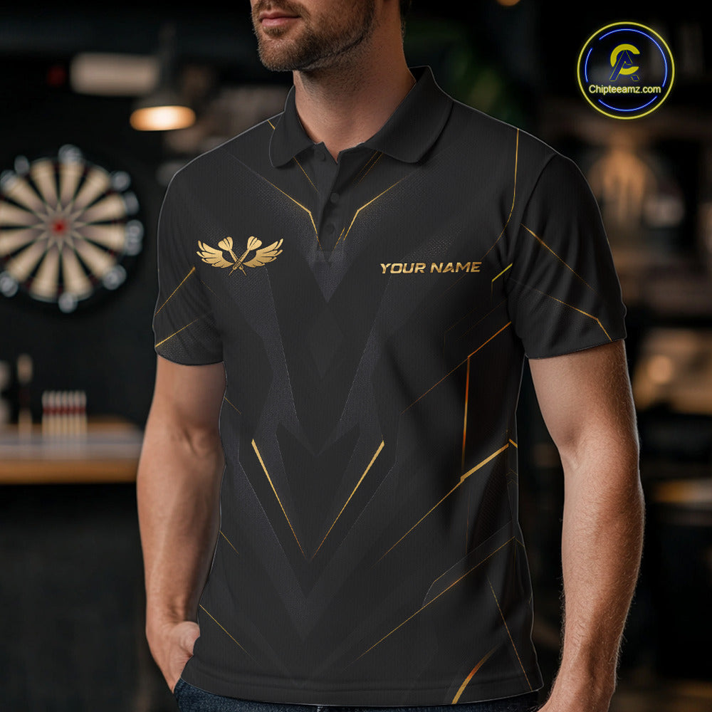 A man wearing a black short-sleeve polo shirt with gold geometric line patterns, a gold winged logo on the left chest, and 'YOUR NAME' printed on the right chest. The background is a blurred bar or sports room setting with a dartboard visible.