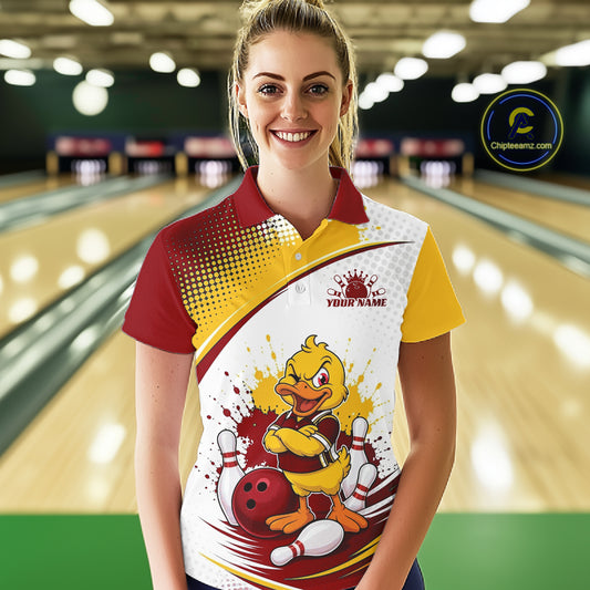 A woman stands in a bowling alley wearing a custom bowling-themed polo shirt. The shirt features a red and yellow collar, a red-to-yellow gradient on the shoulder, and a large cartoon duck mascot graphic on the front with bowling balls and pins.