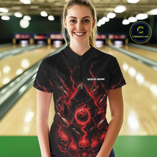 A woman wearing a black bowling-themed short-sleeve quarter zip shirt with a red and black grim reaper graphic and a white 'YOUR NAME' placeholder on the chest, standing in front of a blurred bowling alley background. 