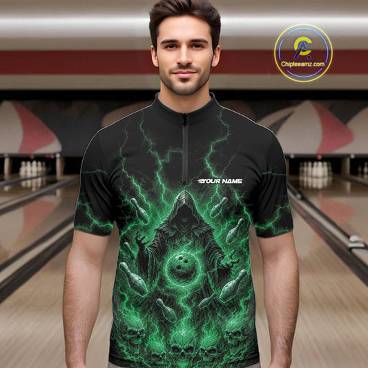 A man wearing a black short-sleeve quarter zip bowling jersey with a vivid green lightning and skull graphic, standing in a bowling alley. 