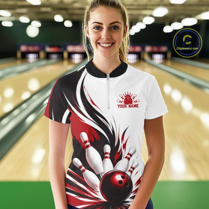 Front view of a female model wearing a white, black, and red bowling quarter zip shirt with a flaming bowling ball and pins illustration at a bowling lane.