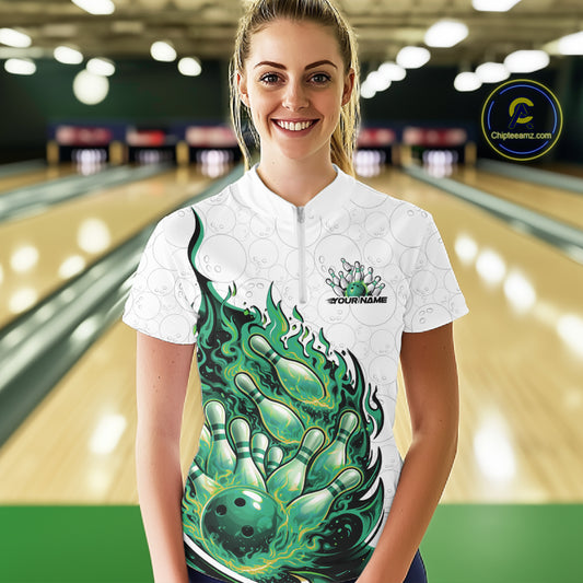 Front view female model at bowling lane wearing white and green quarter zip shirt showing flaming bowling ball crashing into pins with vibrant fire illustration.