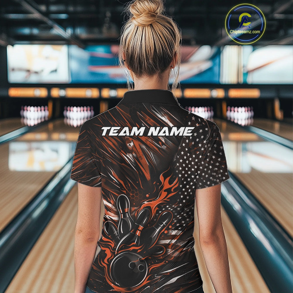 Back view of a female model in a bowling alley wearing a black and orange polo shirt featuring a flaming bowling ball and patriotic bowling motif.