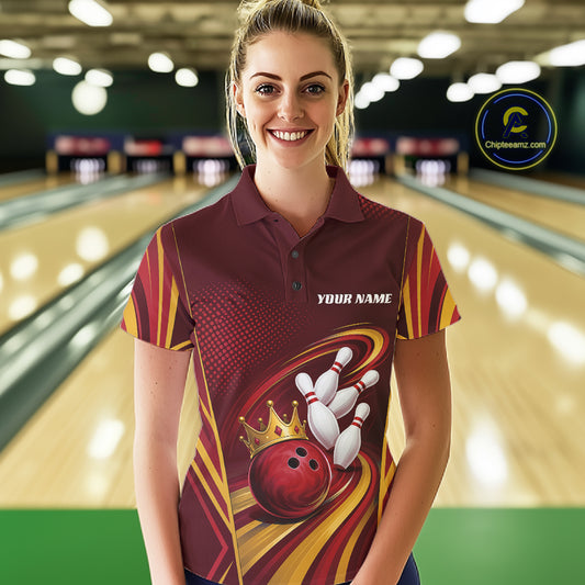 A woman stands in a bowling alley wearing a custom bowling polo shirt. The shirt features a maroon, yellow, and red graphic design with a bowling ball, pins, and a gold crown, along with the text 'YOUR NAME'.
