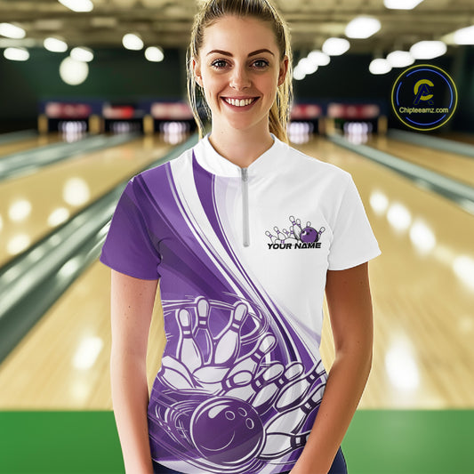 Female model wearing a white and purple bowling quarter zip featuring sweeping curve accents and a bowling ball crashing into pins graphic inside a bowling alley.