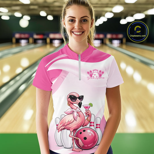 Female model at a bowling lane wearing a pink bowling quarter-zip shirt featuring a stylish flamingo holding a cocktail beside a bowling ball.