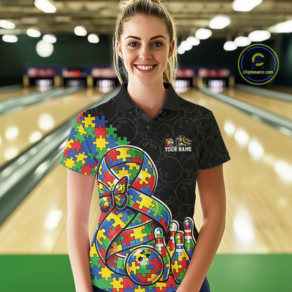 Female model in a bowling lane wearing a black polo shirt, front view showing a large autism awareness ribbon filled with puzzle pattern, colorful butterfly, and bowling ball striking pins artwork