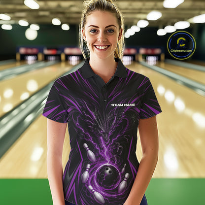 A woman stands in a bowling alley wearing a black short-sleeve polo shirt with a purple and black bowling-themed graphic print. The shirt features a large bowling ball and pins design with purple lightning effects and the text 'TEAM NAME' on the chest.