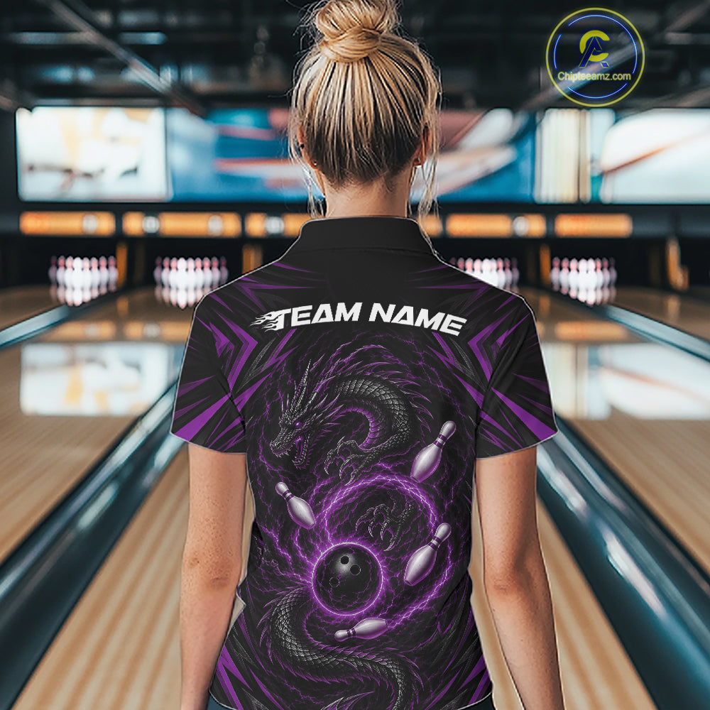 A woman viewed from behind wearing a black short-sleeve bowling shirt with a purple dragon and bowling pin graphic on the back, standing in a bowling alley. The shirt has 'TEAM NAME' printed in white across the upper back.