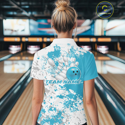 Back view female model in bowling alley wearing white polo with teal blue and white splatter design, relaxed stance near bowling lane