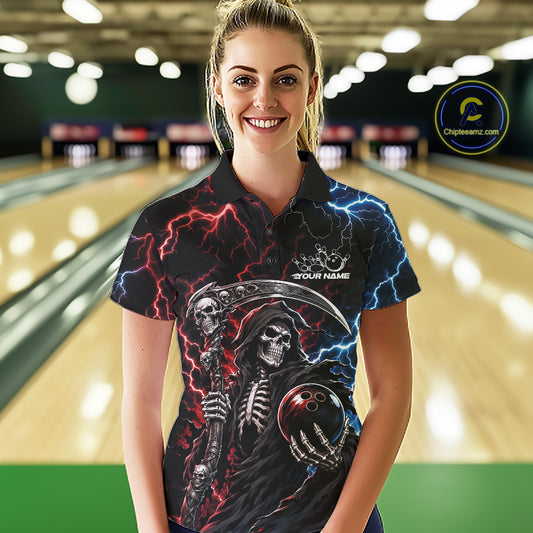 A woman wearing a black short-sleeve bowling shirt with a grim reaper graphic, red and blue lightning, and a bowling ball in the hand, standing in a bowling alley. 