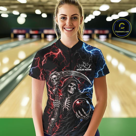 A woman wearing a black short-sleeve bowling shirt with a grim reaper graphic, red and blue lightning effects, and a bowling ball design, standing in a bowling alley. 