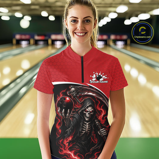 A woman wearing a red and black bowling-themed graphic shirt with a grim reaper design, standing in a bowling alley. The shirt features a red upper section with a subtle pattern, a black lower section with a detailed grim reaper and skull graphic, and a black zipper at the collar.