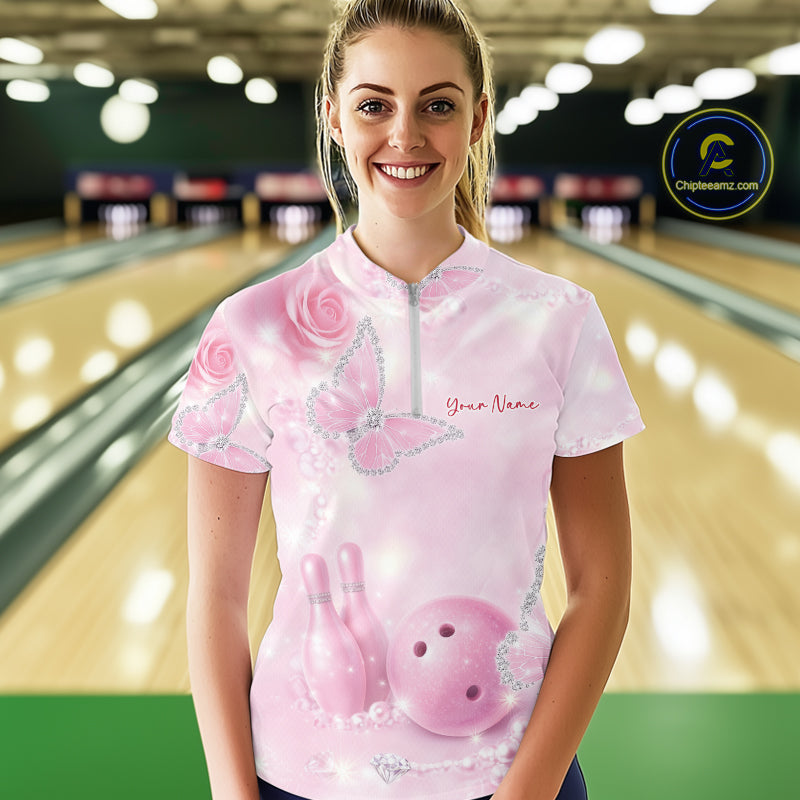 Female model wearing a bowling quarter-zip shirt at the bowling lane with pink glitter butterfly artwork, roses, bowling pins, and a bowling ball on the front.