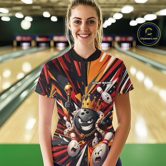 Front view of a female model wearing a black, red, and orange bowling quarter zip shirt featuring a crowned cartoon bowling ball holding a royal scepter with animated bowling pins and colorful burst graphics in a bowling lane.