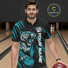 Load image into Gallery viewer, Front view of a male model at a bowling lane wearing a black and teal blue bowling polo shirt featuring a roaring tiger holding a teal blue bowling ball with matching claw-stripe graphics and a geometric background pattern.