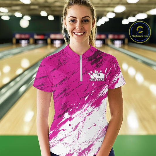 Woman wearing a pink and white bowling shirt with a logo and text in a bowling alley.