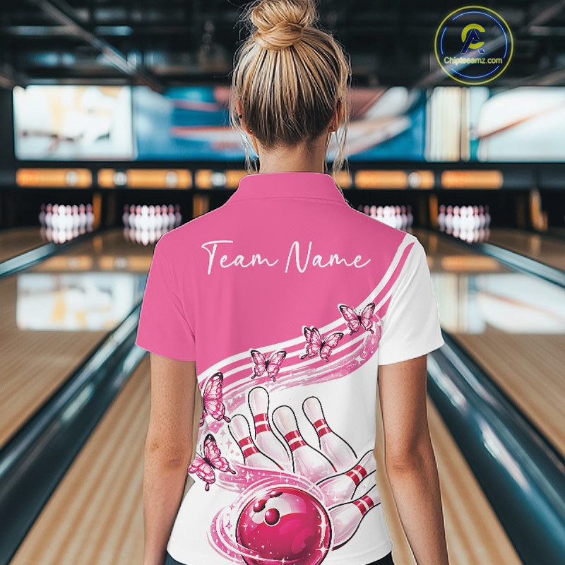 Female model wearing a white and pink bowling polo with butterfly graphics and bowling artwork, back view at the bowling lane