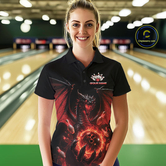 A woman stands in a bowling alley wearing a black short-sleeve polo shirt with a large red and black dragon graphic and a custom logo on the chest. 