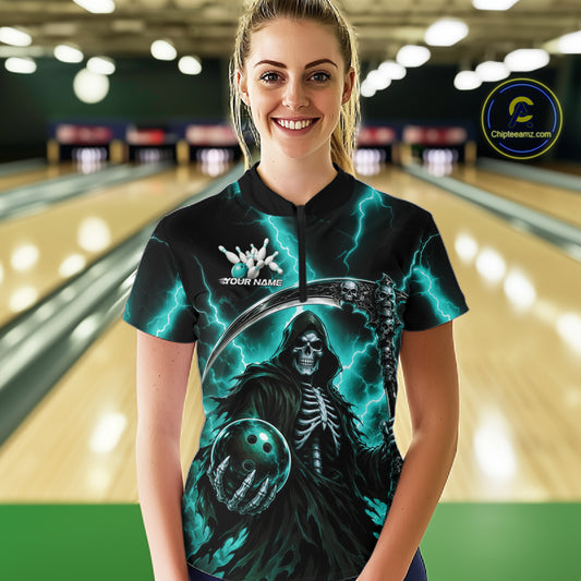 A woman stands in a bowling alley wearing a short-sleeve black bowling shirt with a grim reaper graphic, glowing teal lightning, and a bowling ball illustration. 